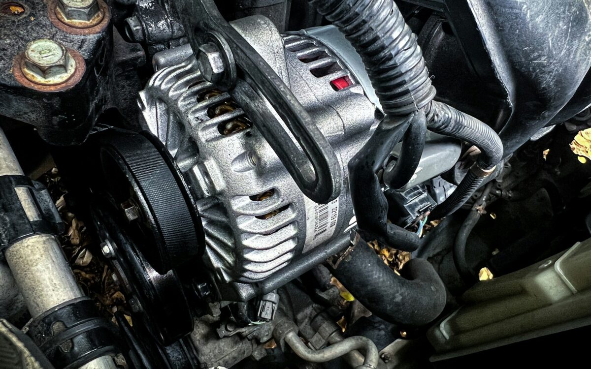 Alternator with its drive belt and pulley in a car engine bay